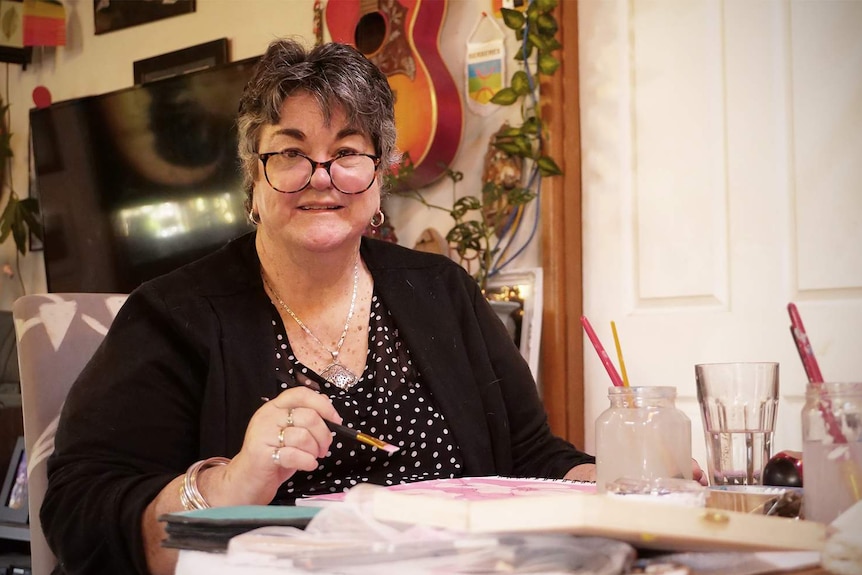 Kim Sattler at her home with a paint brush in her hand, painting a water colour.