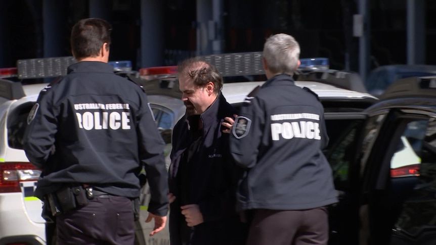 A man is escorted out of a car by two police officers.