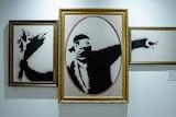 A Banksy mural of a man throwing a bunch of flowers is pictured inside three gold frames.