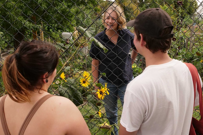 A woman looks through a fence and talks to a man and woman on the other side.