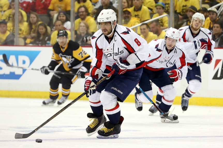 A hockey player pushes the puck along the ice rink followed by teammates