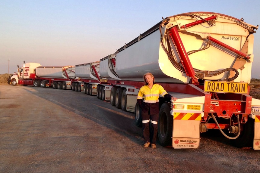Lyndal Denny stands in a workwear at the back of a large road train against an outback background