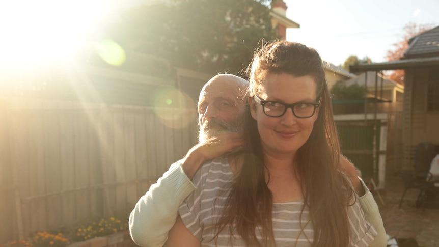 An older man hugs a young woman in the sunshine in a suburban backyard