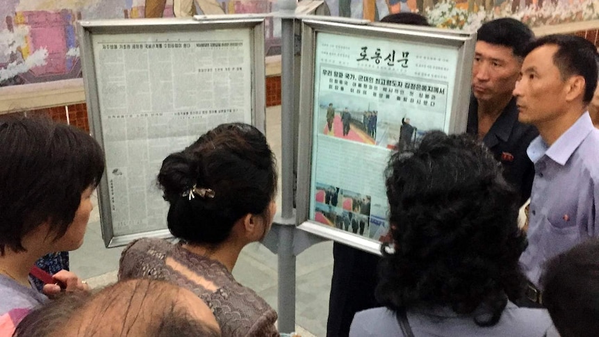 Korean residents look at a news paper sign.
