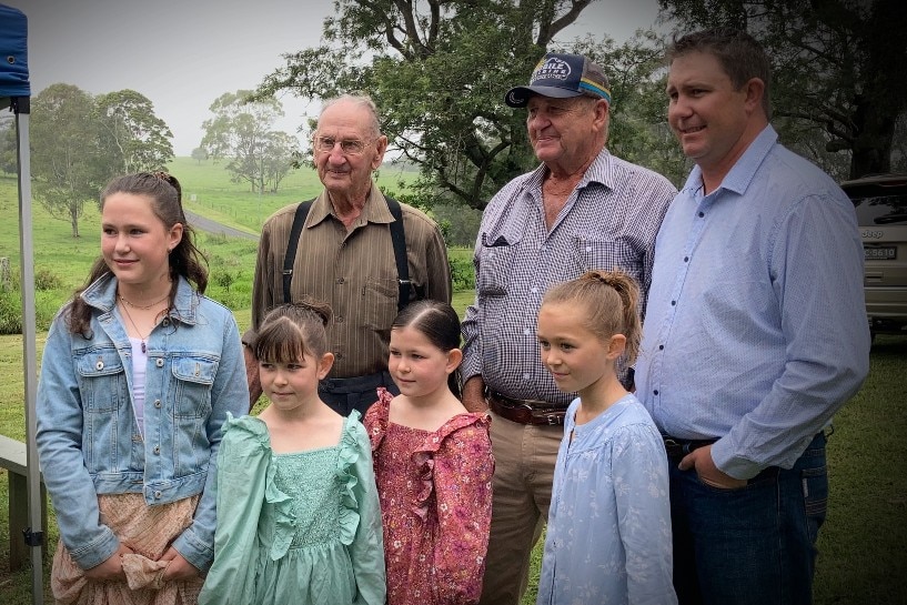 92 year old man standing with four generations of family, rural backdrop