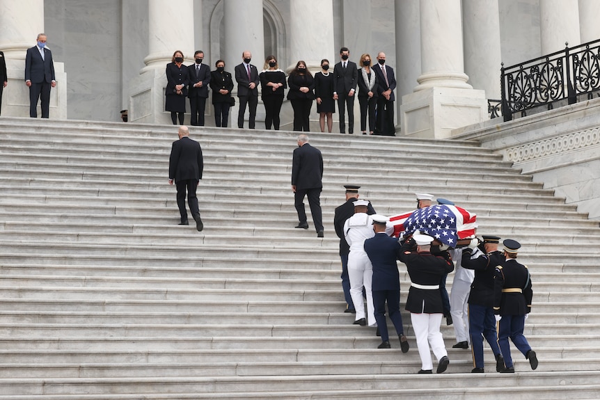Men in uniform walk a coffin draped in the US flag up steps.