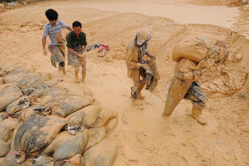 Four men covered in yellow mud carry materials.