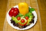 A plate with lettuce leaves with a smiley face made up of tomato and capscium.