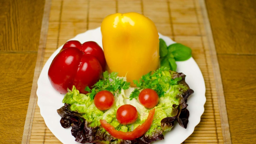 A plate with lettuce leaves with a smiley face made up of tomato and capscium.