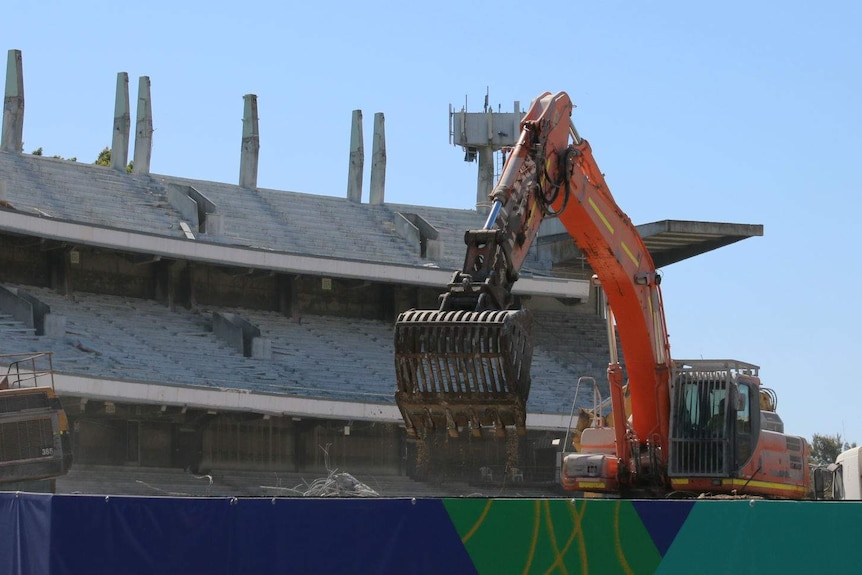 A construction vehicle picks up rubble with the remains of the old Subiaco Oval grandstand in the background.