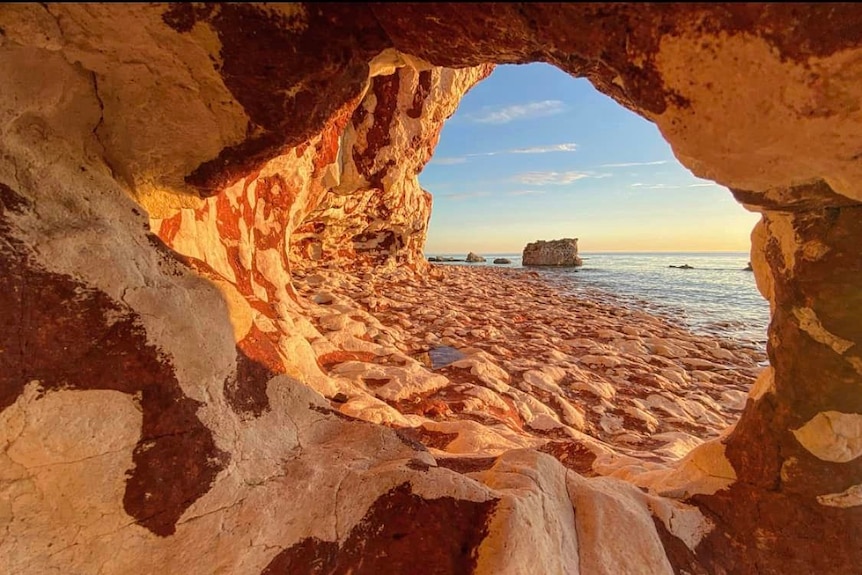 A view through a tunnel of rocks with the ocean in the background.