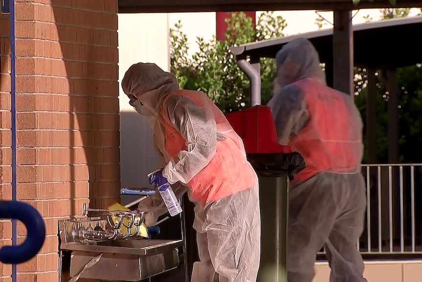 People in personal protective equipment wipe down railings and bubblers at South Strahfield Public School.