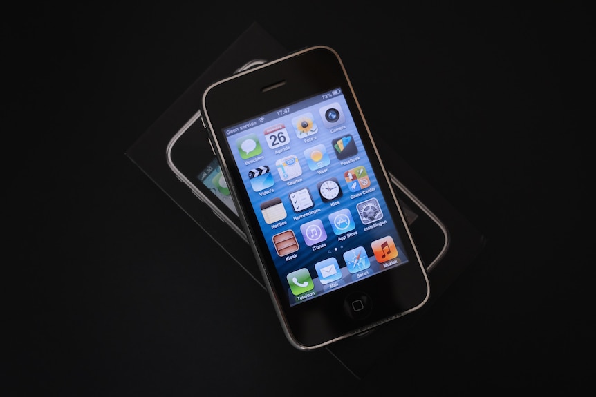 An old Apple iPhone 3GS lying on top of its box on a black background.