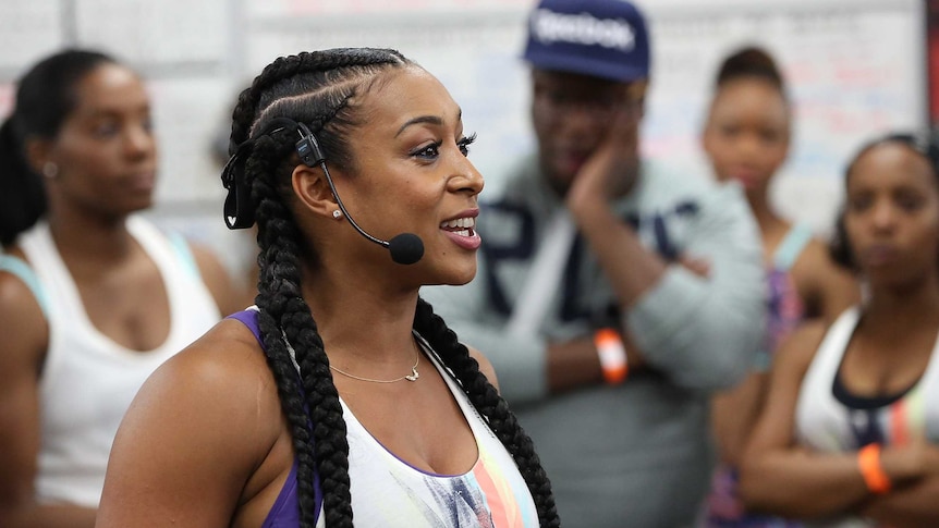 A smiling woman with braids wearing sports gear.