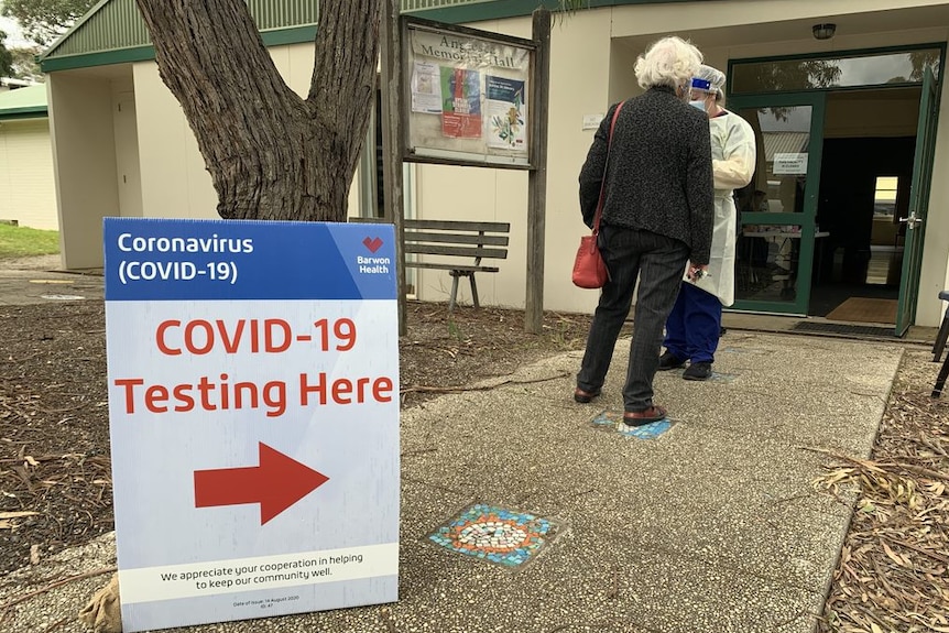 A COVID-19 testing sign outside a building with two women standing nearby.