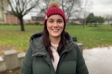 A woman wearing a beanie stands in a park.