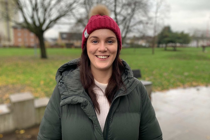 A woman wearing a beanie stands in a park.