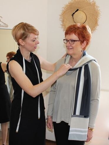 Fashion designer Michelle Kent draping a scarf over a client's neck in a fitting room.