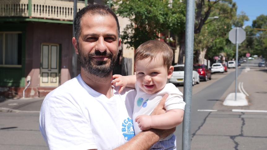 A man and a 8-month-old look into the camera at a suburban intersection