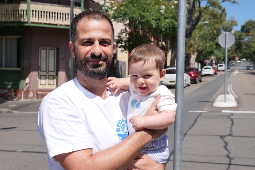 A man and a 8-month-old look into the camera at a suburban intersection