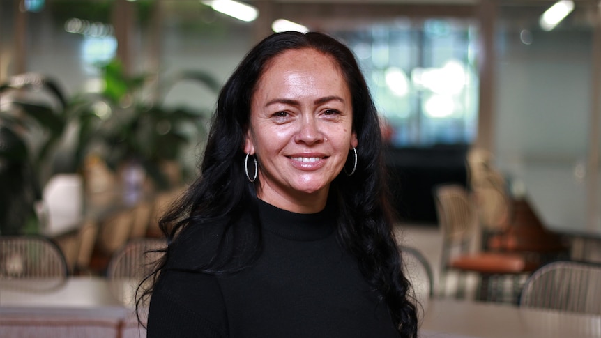 Moana smiling and wearing a black top in a portrait.