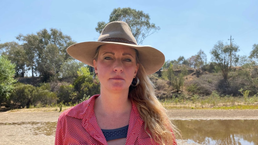Veronica looks into the camera, standing near a shallow dam and wearing a protective hat.