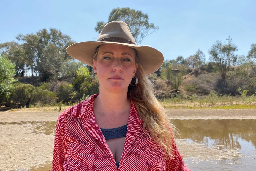 Veronica looks into the camera, standing near a shallow dam and wearing a protective hat.