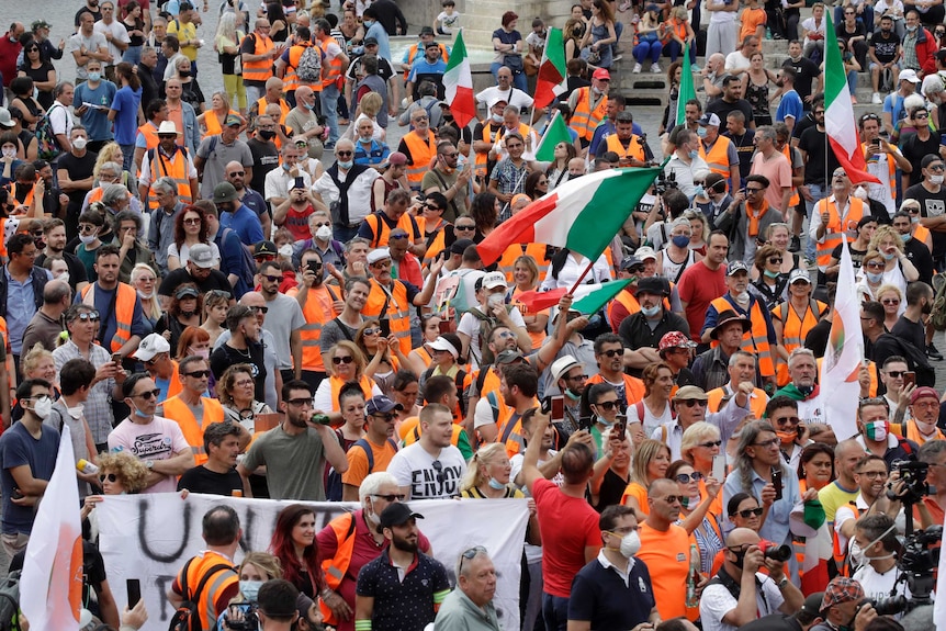 A crowd of people, many wearing orange high-vis vests stand together.
