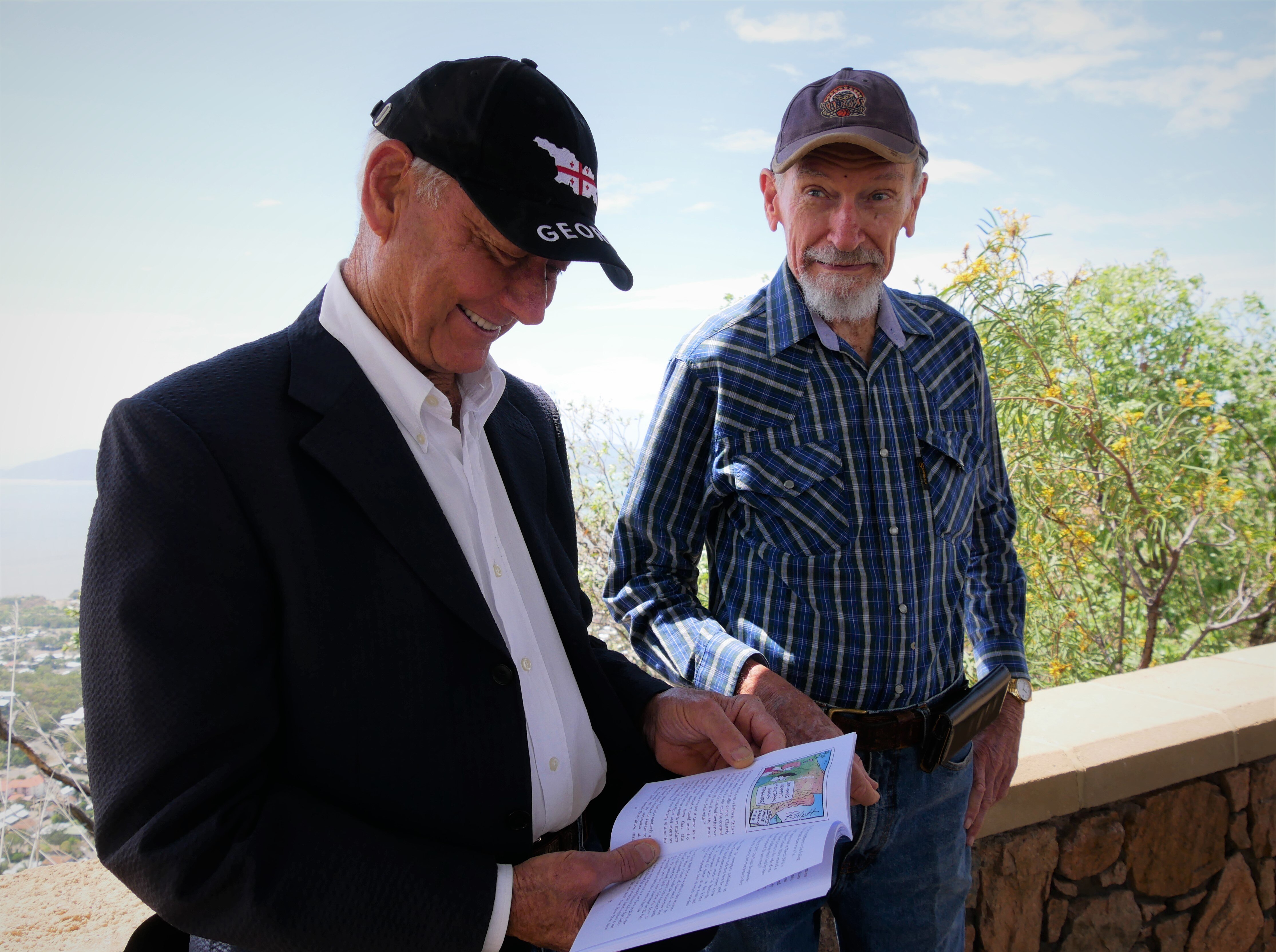 Two men look at a book smiling