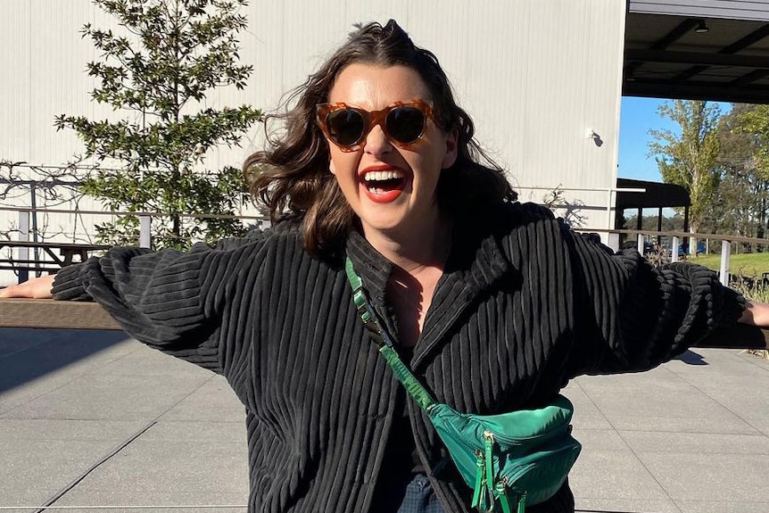 A smiling woman wearing sunglasses hanging from a fence rail.