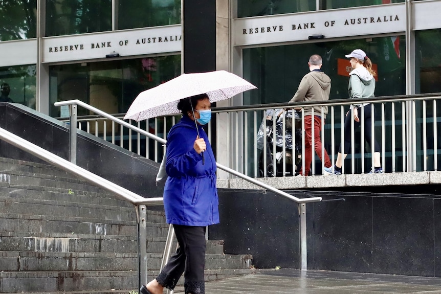 Kobieta otwiera parasol przechodząc przed siedzibą Banku Rezerw Australii w Martin Place w Sydney.