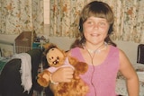 An old photo of a little girl with brown hair holding a stuffed toy