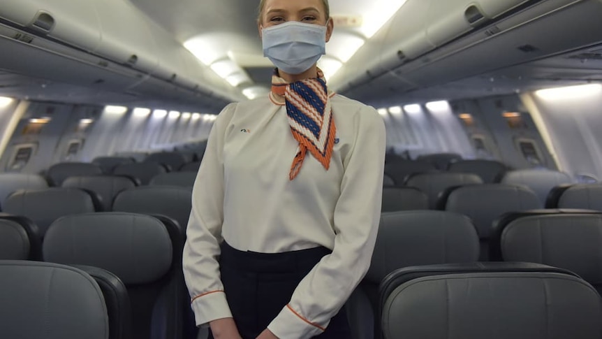 A masked, female flight attendant on a plane.