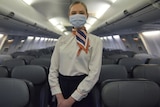 A masked, female flight attendant on a plane.