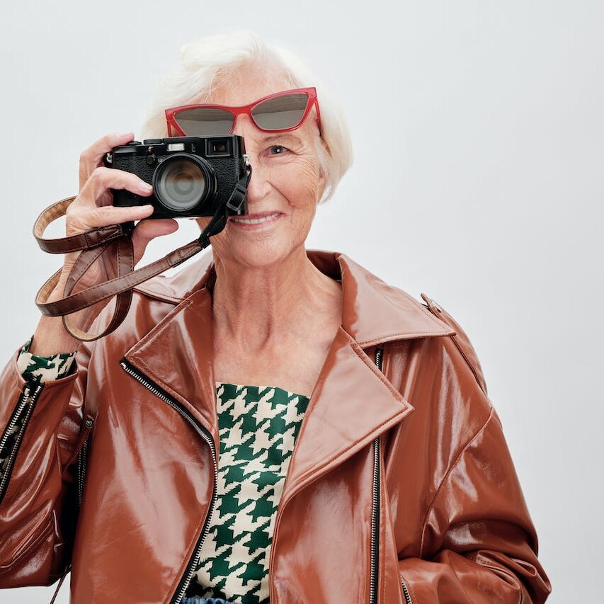 An older woman is holding a camera to one eye looking through it