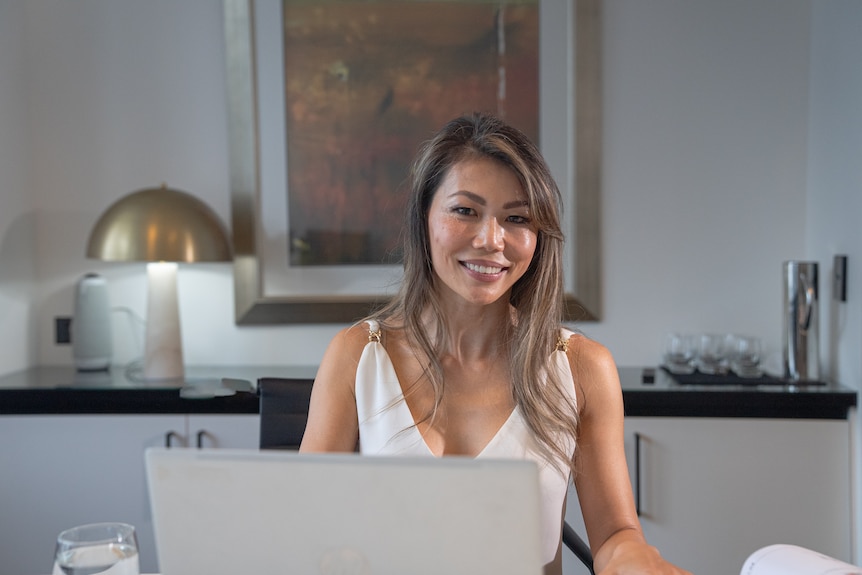 A woman, of Asian descent, looks towards the camera, while working at her office desk.