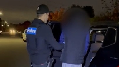 A Victoria Police officer leads an attempted murder suspect into a police car.