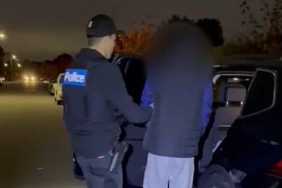 A Victoria Police officer leads an attempted murder suspect into a police car.