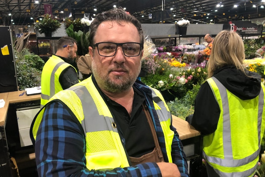 A man wearing high vis stands in a flower market.