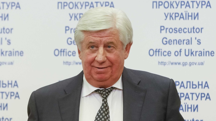 A man standing in front of a sign reading "Prosecutor General's Office of Ukraine"