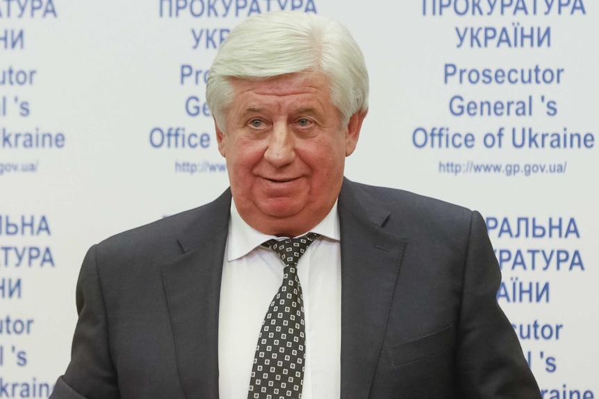 A man standing in front of a sign reading "Prosecutor General's Office of Ukraine"