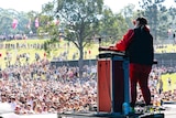 A woman behind a podium in front of a microphone in front of a crowd