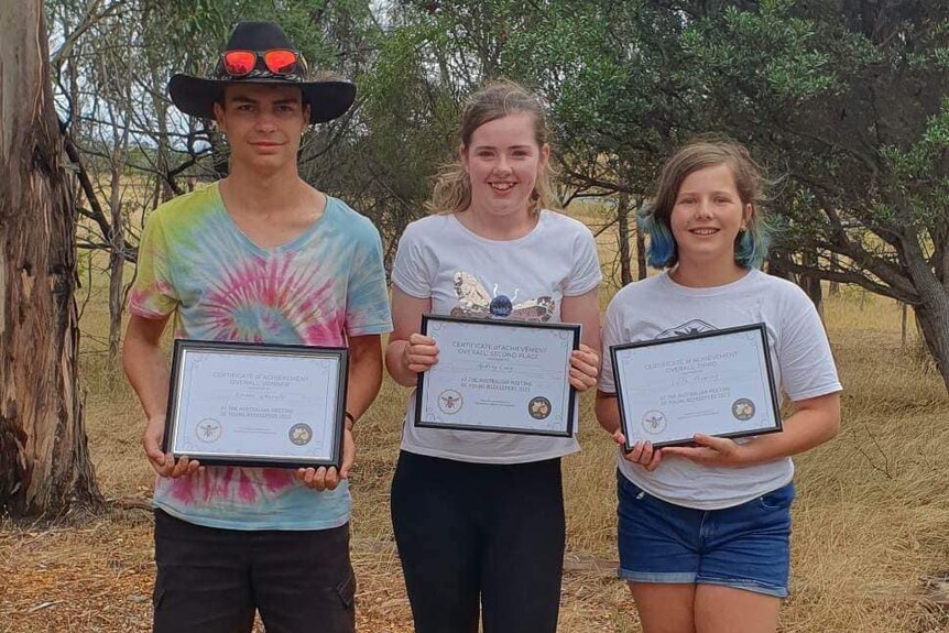 Three young people smiling holding certificates.