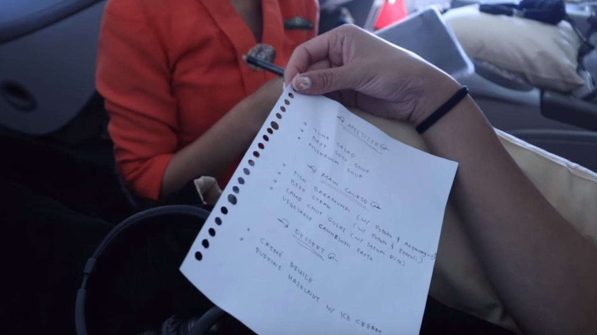 A person holds a hand-written menu while sitting on a plane.