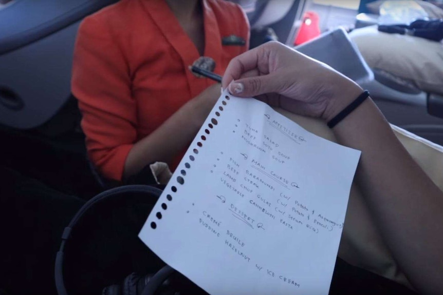 A person holds a hand-written menu while sitting on a plane.
