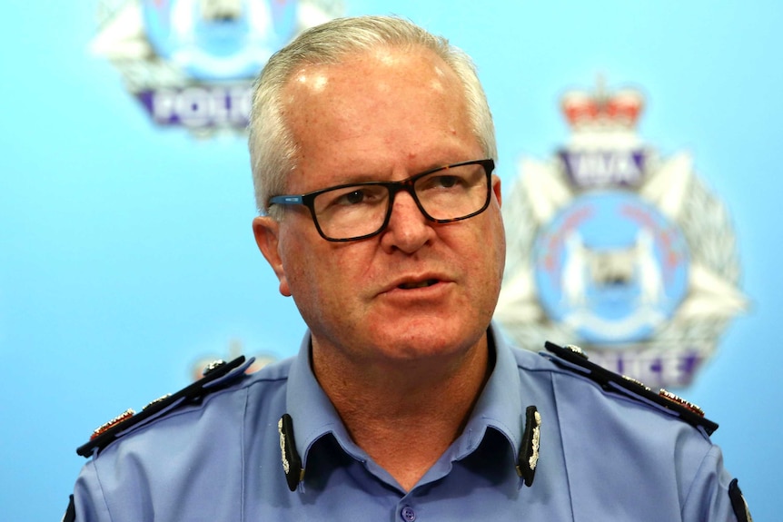 Mr Dawson speaks in front of a wall with the WA police logo on it.