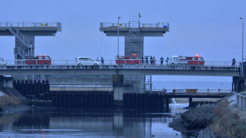 People keep a lookout at the mouth of a river after tsunami advisories triggered by an earthquake were issued.