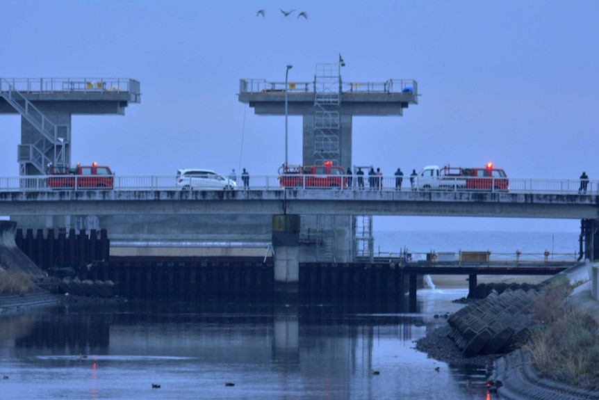 People keep a lookout at the mouth of a river after tsunami advisories triggered by an earthquake were issued.