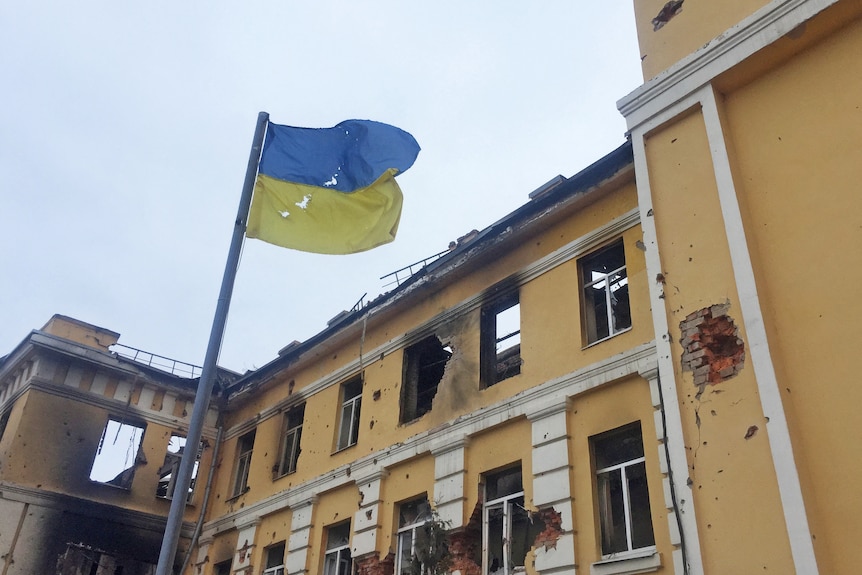 The fascade of a school in Kharkic had large holes from apparent shelling damage, Ukrainian flag waves in the foreground.