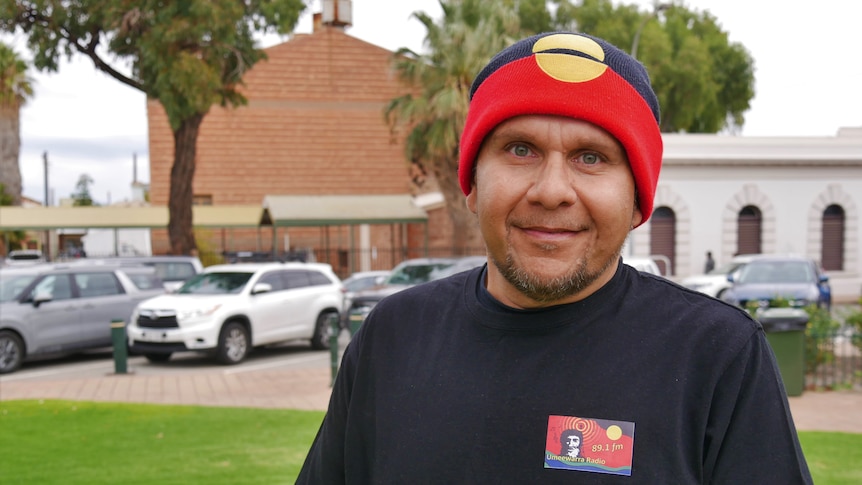 An indigenous man wearing a black shirt and an Aboriginal flag themed beanie 